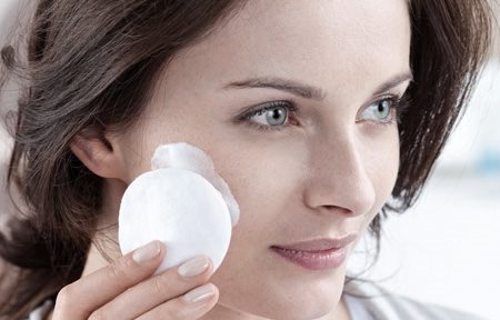 Жена нанася крем по лицето си с помощта на памучен тампон