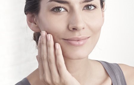 Жена нанася крем на лицето си 