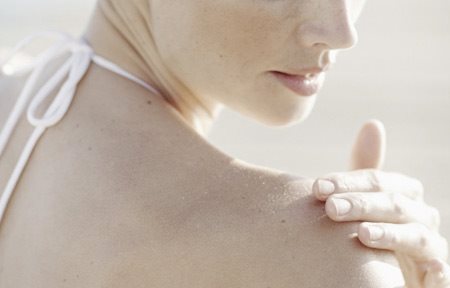 Жена нанася крем по дясното си рамо.